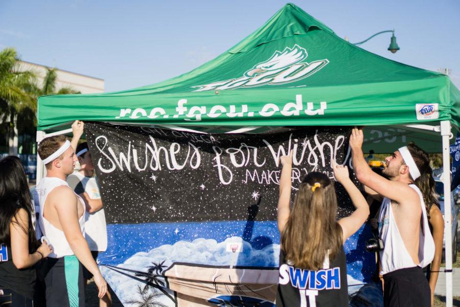 Members of the Chi Omega sorority hang up a Swishes for Wishes banner with the help of a couple of participants. (EN Photo / Zack Rothman)
