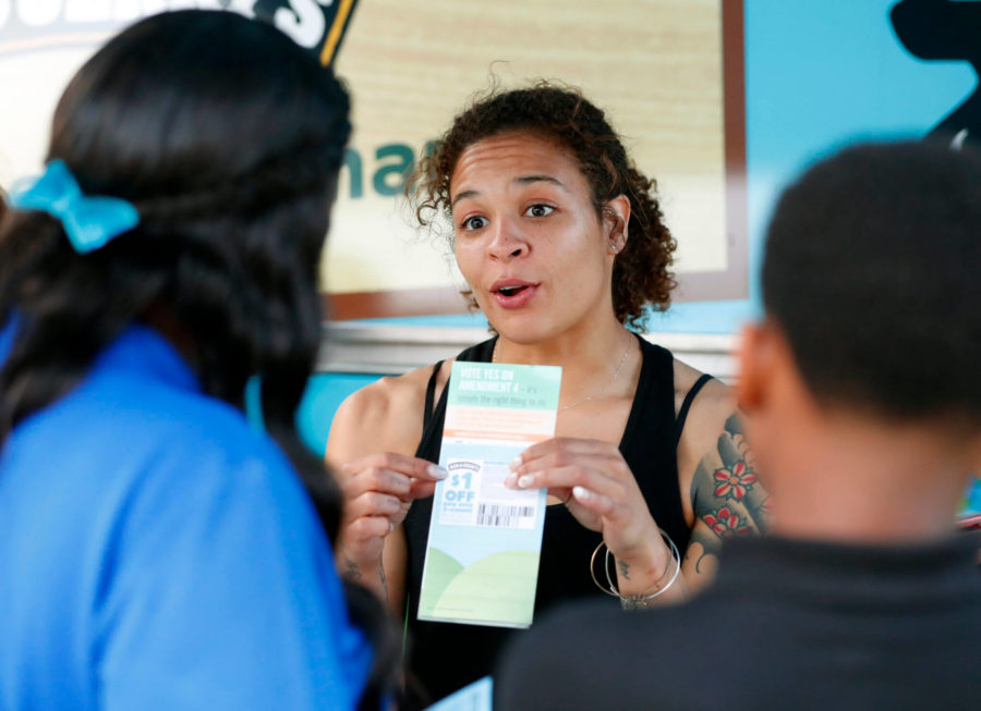In this, Monday, Oct. 22, 2018 photo, Jessica Jones, center, speaks to people gathered around the Ben & Jerrys Yes on 4 Truck about Amendment 4 at Charles Hadley Park in Miami. Amendment 4, asks voters to restore the voting rights of people with past felony convictions. More than 1.5 million adults in Florida are ineligible to vote because they have felony convictions.  (AP Photo/Wilfredo Lee)