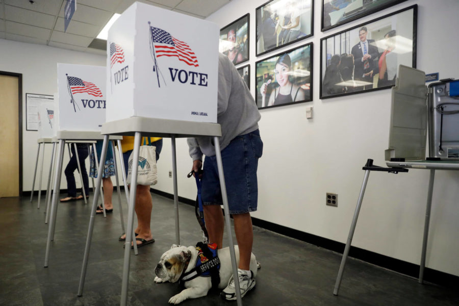 Tom Brezinski, at right, votes while his service dog Suzie lays at his feet at the Los Angeles County Registrar of Voters office Tuesday, Oct. 23, 2018, in Norwalk, Calif. The general election takes place on Nov. 6th. (AP Photo/Marcio Jose Sanchez)