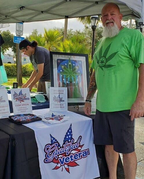 EN Photo by Brooke Stiles. Veteran, Jeffrey Demond, stands next to The Grateful Veteran tent at an event. In 2018, DeMond created The Grateful Veteran, a non-profit organization focused on educating veterans about medical cannabis as an alternative to pharmaceuticals. Demond and the organization run on the belief that alternative medicine can significantly decrease veteran deaths by overdose and suicide.