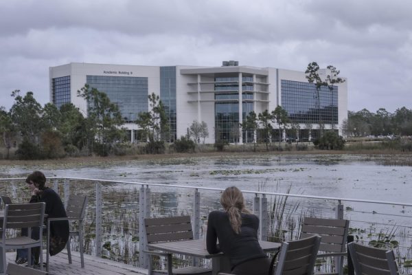 Students sit outside of the library at tables overlooking a pond and the Water School. Photo by Alo Zarate. 